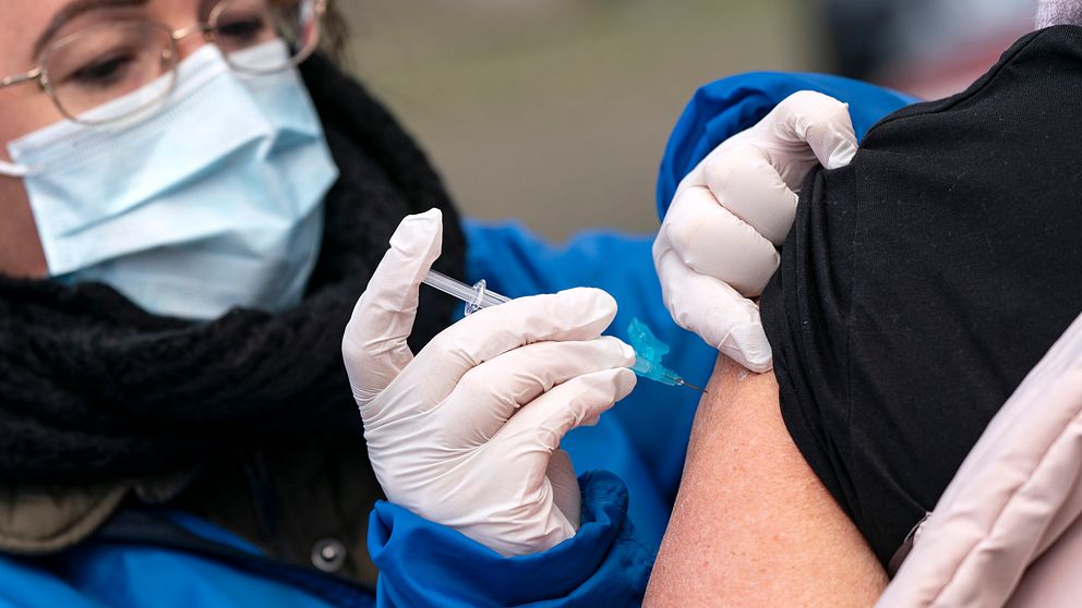 Kvinna med munskydd ger en vaccinspruta.