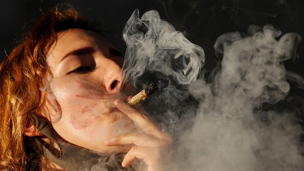 Närbild på kvinna som röker en stor marijuanacigarett som skapar ett stort rökmoln.