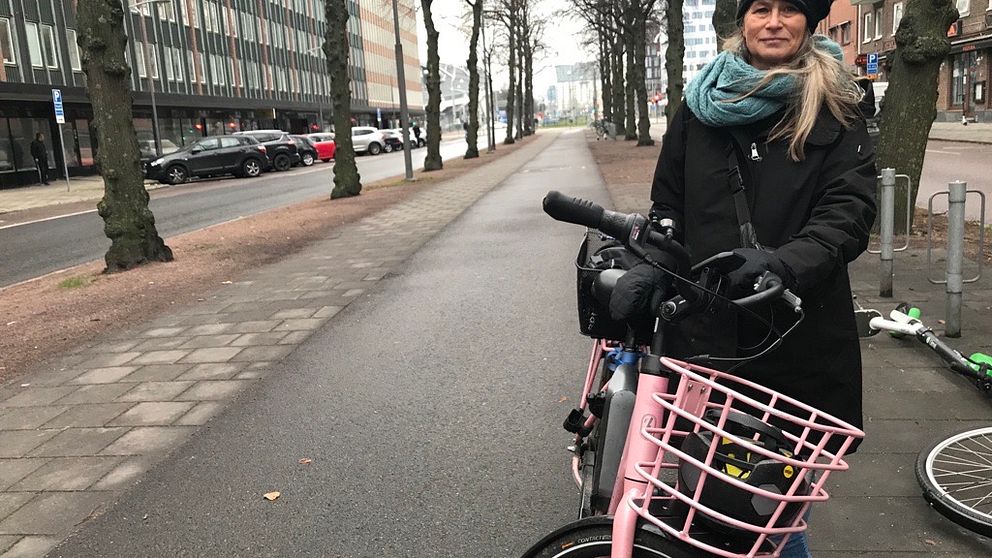 Kvinna med randig mössa och blå halsduk håller i sin rosa cykel.