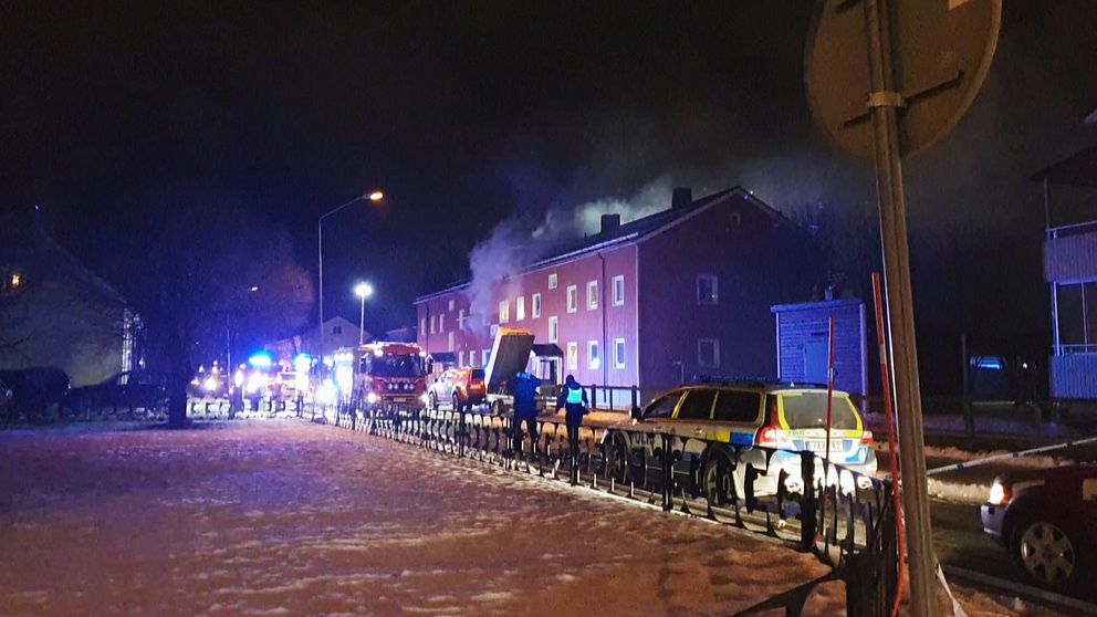 Ett rött hus brinner. Det kommer grårök ur fönster. Flera brandbilar på plats.