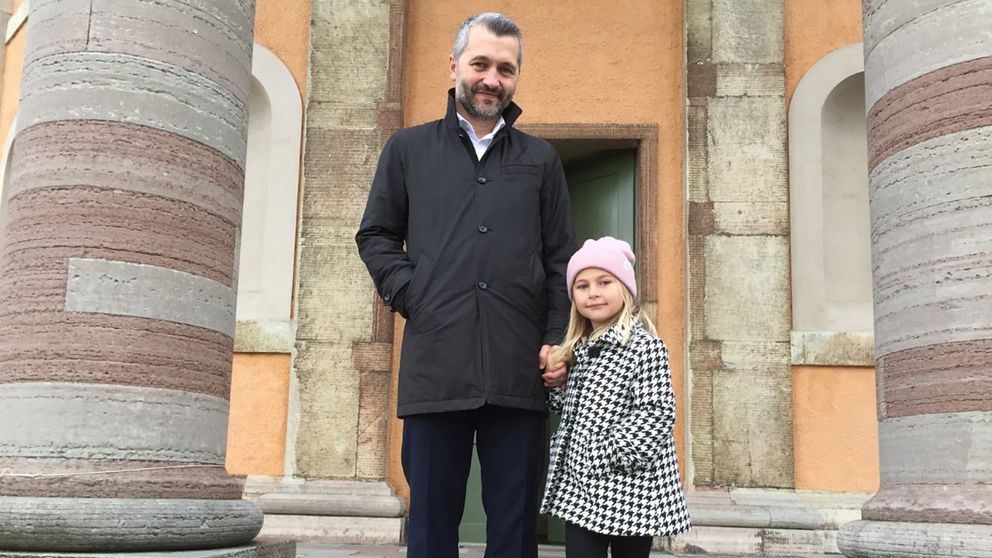 En medelålders man och en liten flicka står framför en kyrkport.