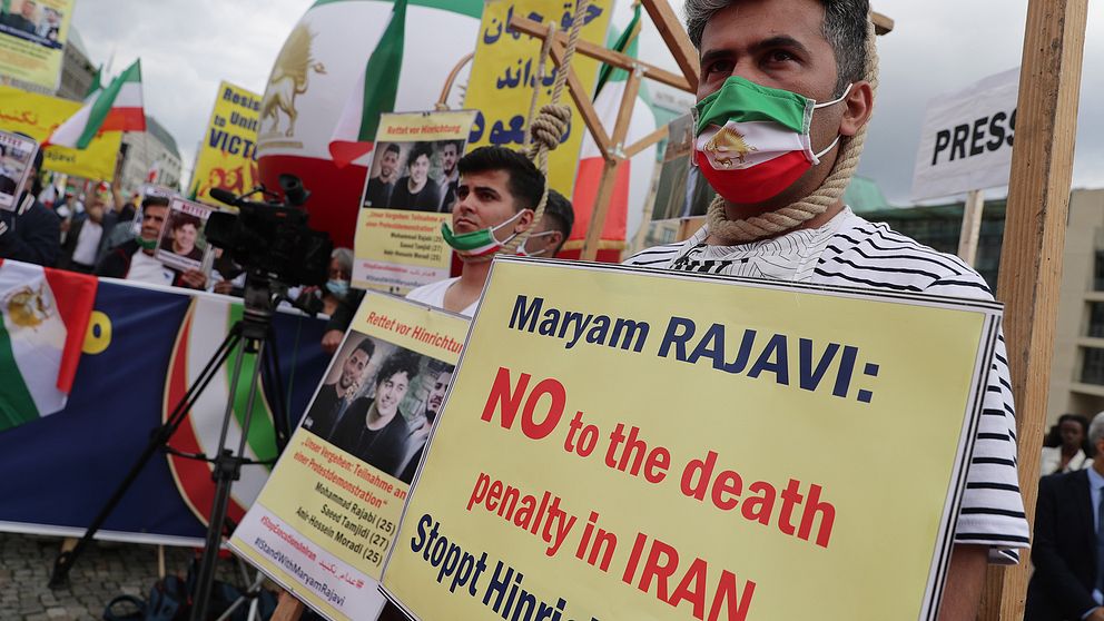 En man med munkskydd i iranska flaggans färger håller ett plakat med texten ”nej till dödsstraff i Iran” under en demonstration i Tyskland i juli 2020.