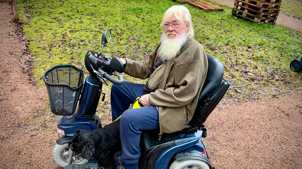 en äldre man i trehjulig elrullstol med styre, ute på sin gård