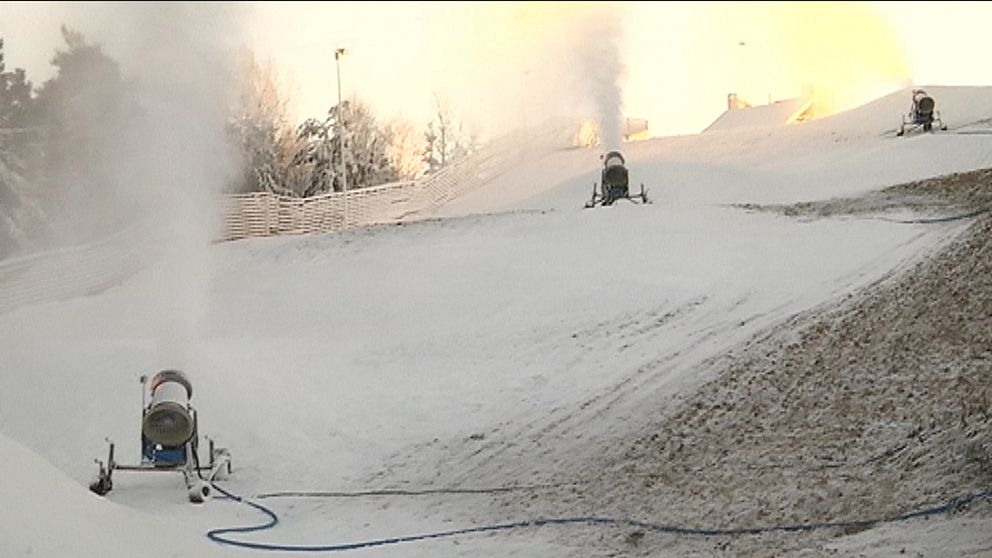 tre snökanoner sprutar ut snö på en delvis bar skidbacke