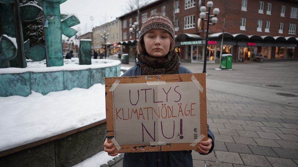 En ung kvinna håller i en skylt med texten: ”Utlys klimatnödläge nu!