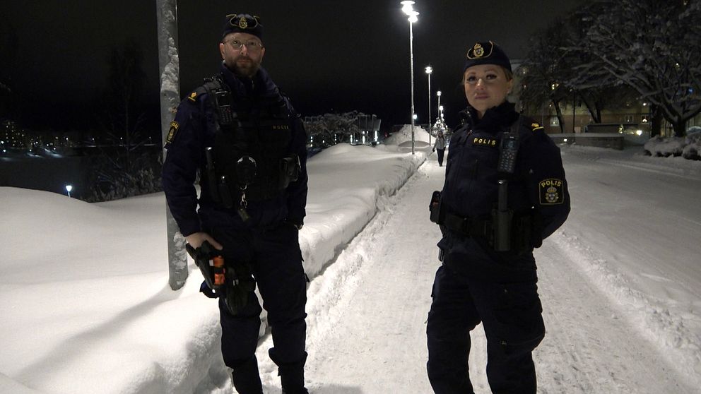 två poliser i unifrom på en snöig gågata upplyst av gatlampor