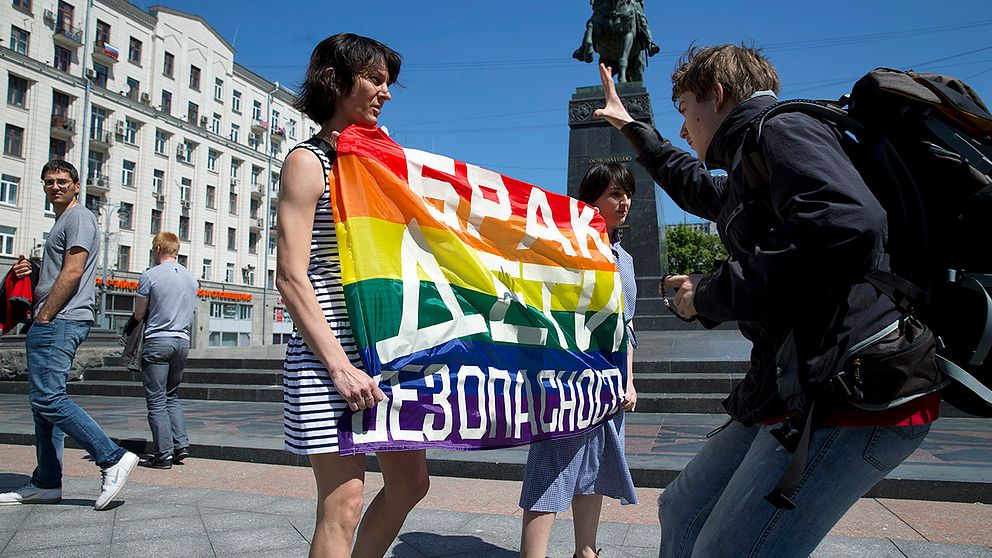 En man försöker dra åt sig en banner med texten ”Äktenskap, barn, trygghet” som två gayrättsaktivister håller upp i samband med en Pridemanifestation i Rysslands huvudstad Moskva i maj förra året.