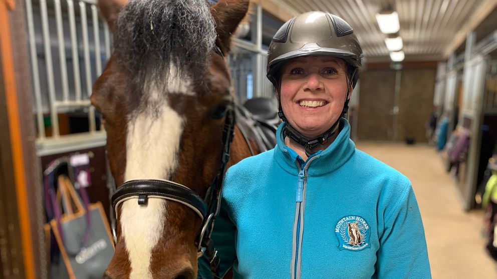 Vicky Pettersson, ridskolechef Mora Ridklubb, står i stallet bredvid en brun häst.