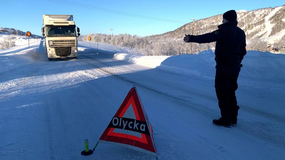 Polis står och visar in en lastbil på en parkeringsyta. Vinter. En skylt med texten ”olycka” står på vägen.