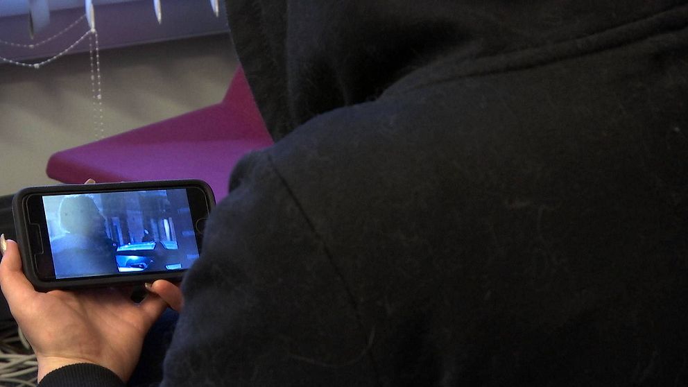 En kvinna med svart luvtröja tittar på ett klipp i en mobiltelefon.