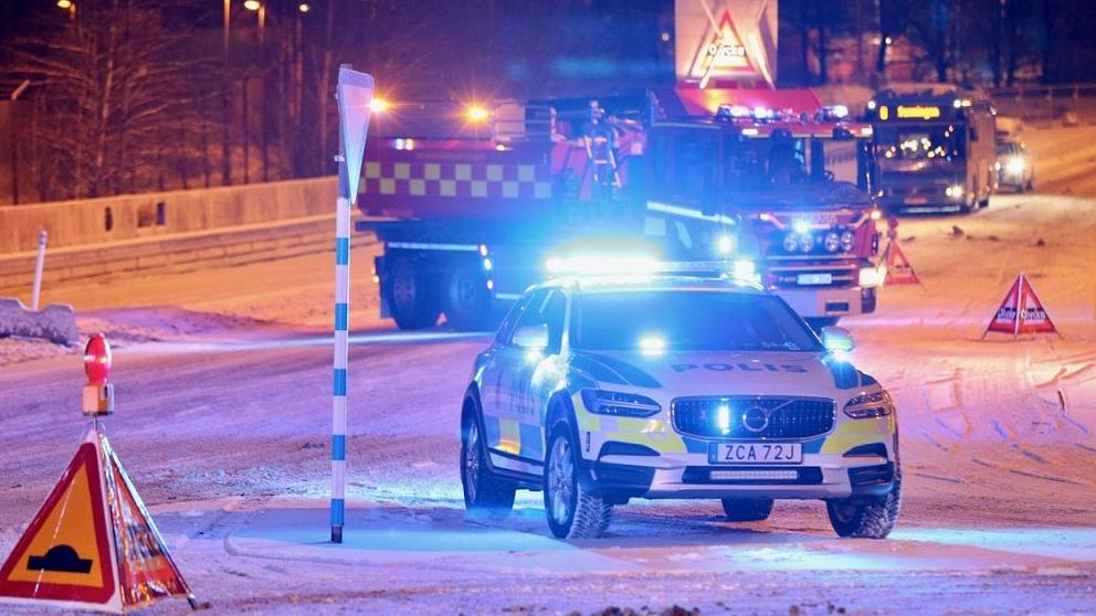 Polisbil i förgrunden. Skyltar om olycka. Brandbil i bakgrunden. Snöigt underlag.