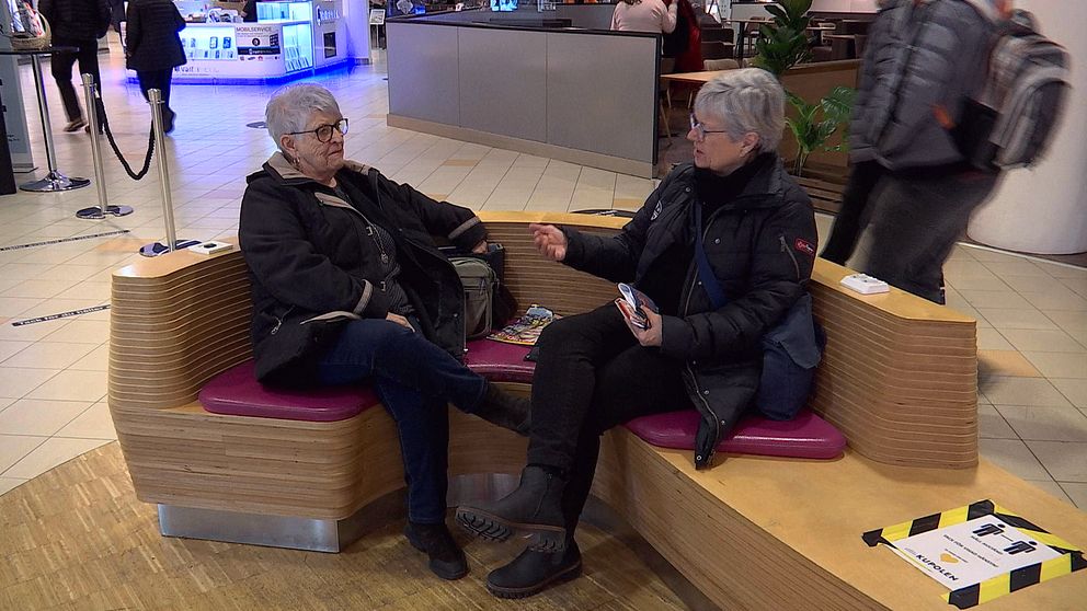 Lena och Rose-Marie Asplind sitter på en bänk i ett köpcentrum.