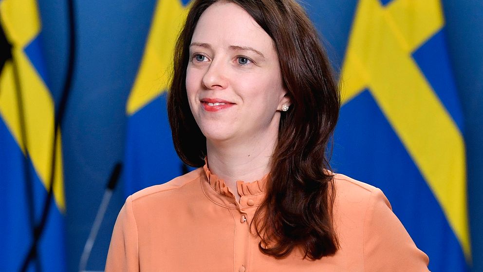 Bilden visar Åsa Lindhagen (MP) som blir finansmarknadsminister och biträdande finansminister. Här står hon i korallfärgad blus framför tre svenska flaggor.
