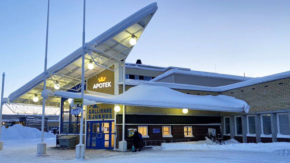 Stor byggnad i gult tegel med snö på taket. Ovanför dörren står det Gällivare sjukhus och Apotek.