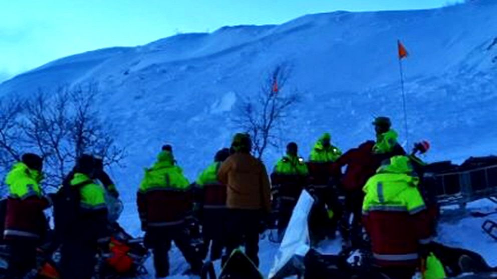 Flera personer med varselkläder som står framför en fjällsida.