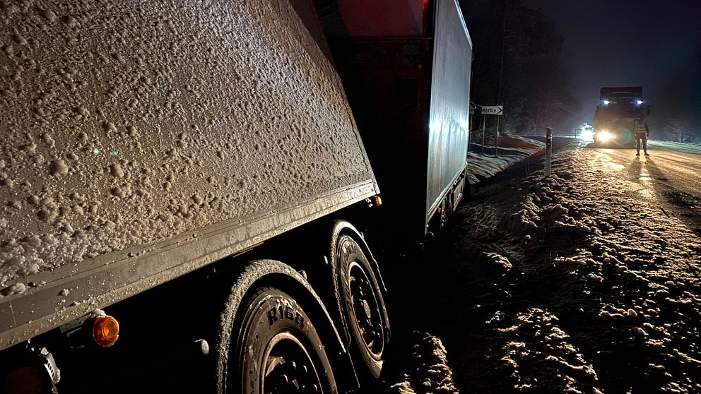 Bilden föreställer en lastbil som ligger i diket. På vänster sida i bakgrunden syns ett räddningsfordon. Framför det står en person i reflexväst.