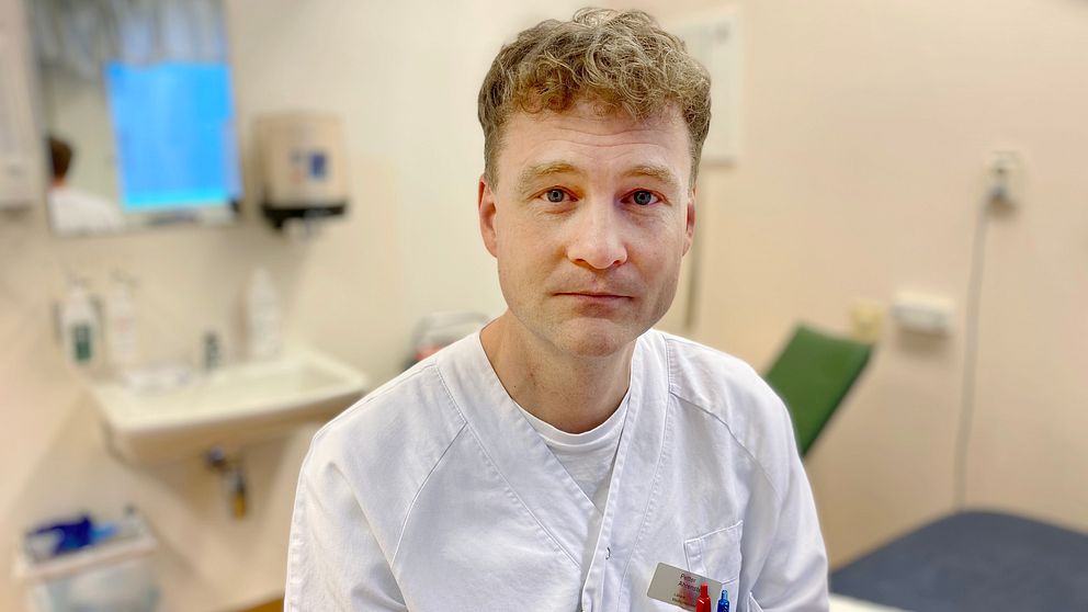 Petter Ahrensted i vita läkarkläder sitter på en brits i ett undersökningsrum.