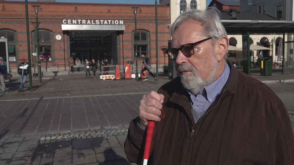 Blind man med glasögon och käpp framför centralstationen i Malmö.