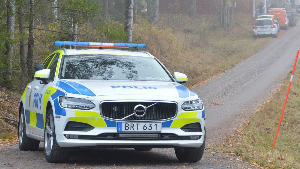 polisbild i förgrund, grusväg in mot fastighet med flera fordon