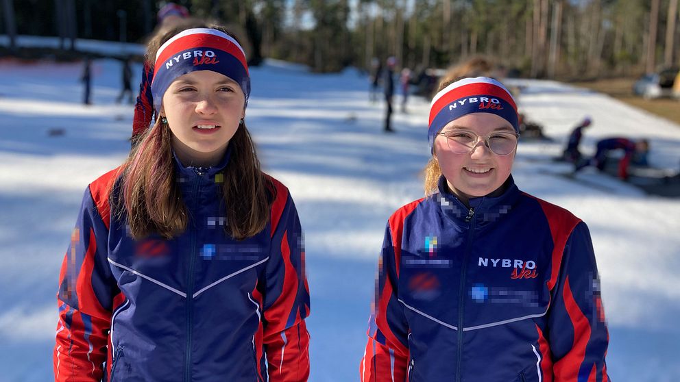 Bild på två flickor som står bredvid varandra i blåröda träningsoveraller och pannband. I bakgrunden syns snö-