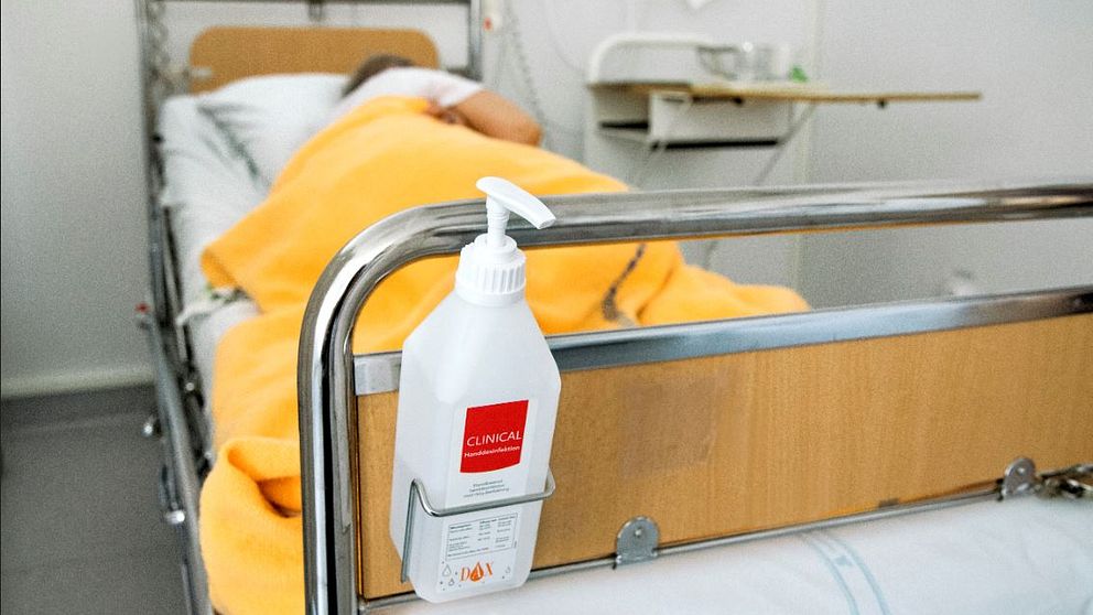 En flaska handsprit som fästs på en sjukhussäng där det ligger en patient.