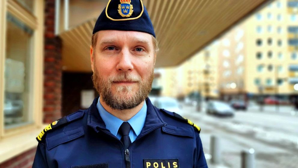 Bilden är ett porträtt av lokalpolisområdeschefen Josef Wiklund utomhus. Josef Wiklund har polisuniform på sig och i bakgrunden syns bilar och en gata samt bostadshus.