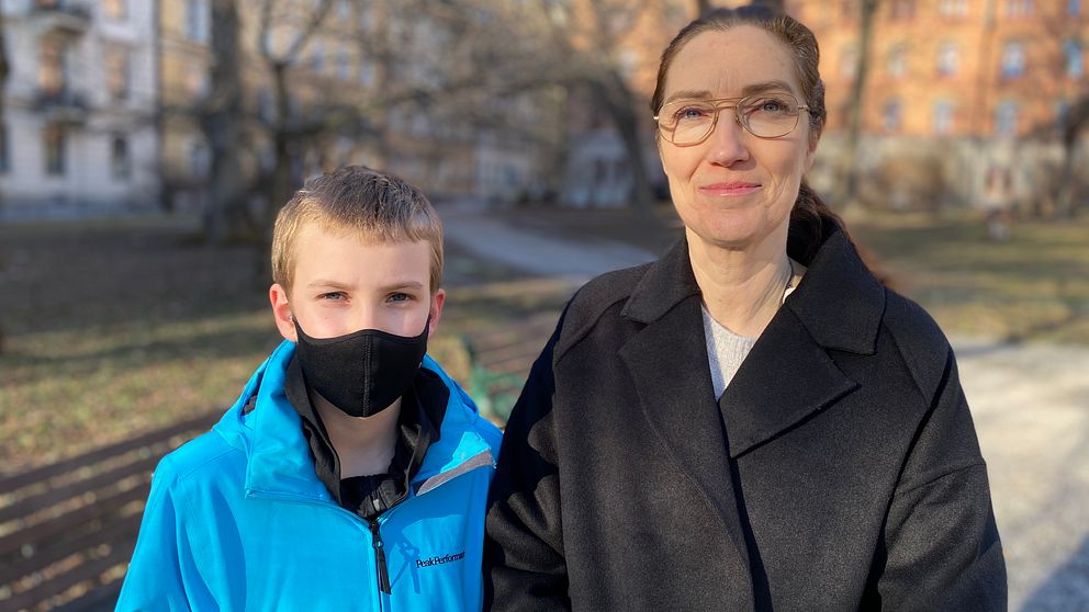 Linus har en blå jacka och ett svart munskydd på sig. Brevid står hans mamma Sarah, hon har en svart jacka och glasögon. De är i fokus medan bakgrunden är lite suddig.