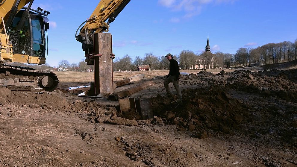 grävskopa och man som utför grundläggningsarbete med klosterkyrkan i barkgrunden