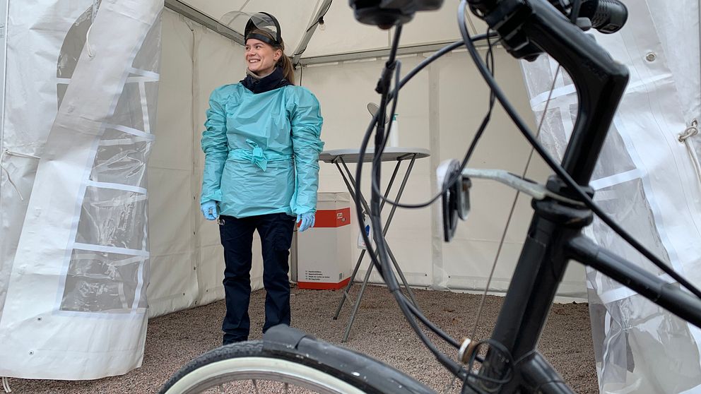 En cykel i förgrunden och en ung kvinna i ett provtagningstält i bakgrunden, hon har skyddskläder på sig.