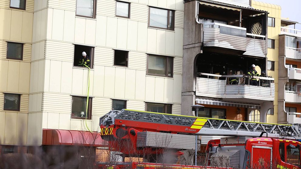Brandmän på en balkong i ett lägenhetshus. Spår av brand på balkongen.