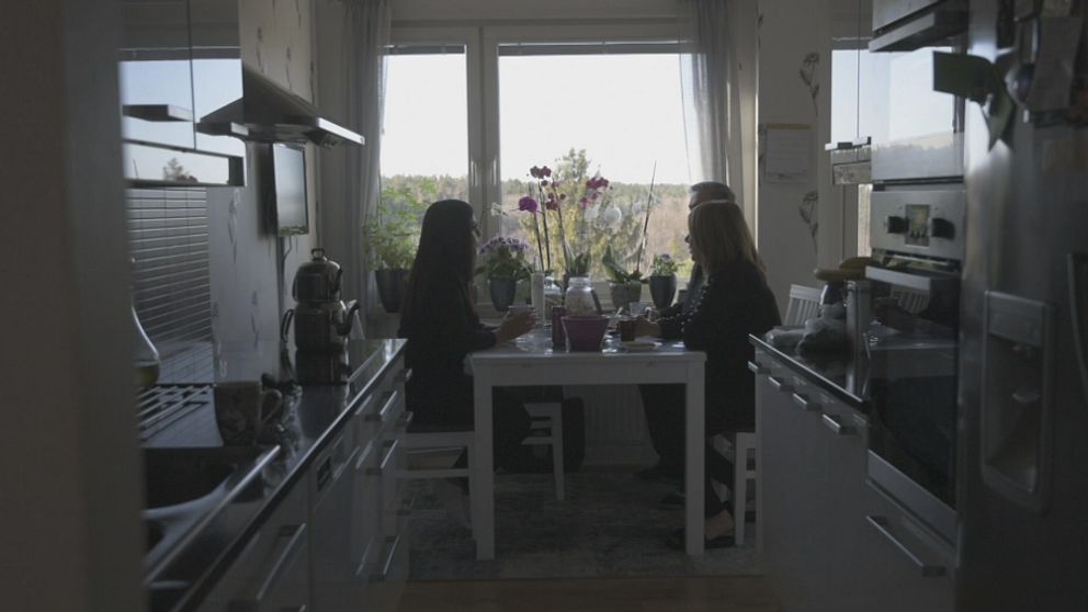 Tre personer sitter vid ett matbord i ett kök.