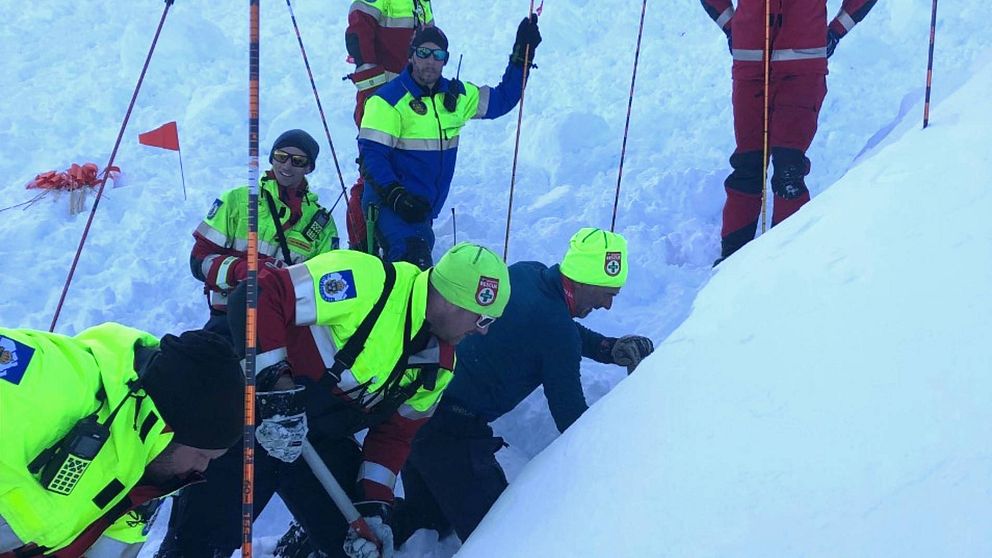 flera personer i fjällräddningens varselkläder som gräver i backe där lavin gått, några med sond (stav)