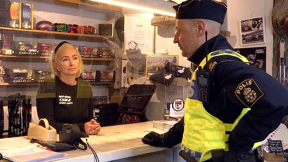 en kvinna bakom den kassadisk, goggles på hyllan bakom, samt en man i poliskläder som pratar med henne