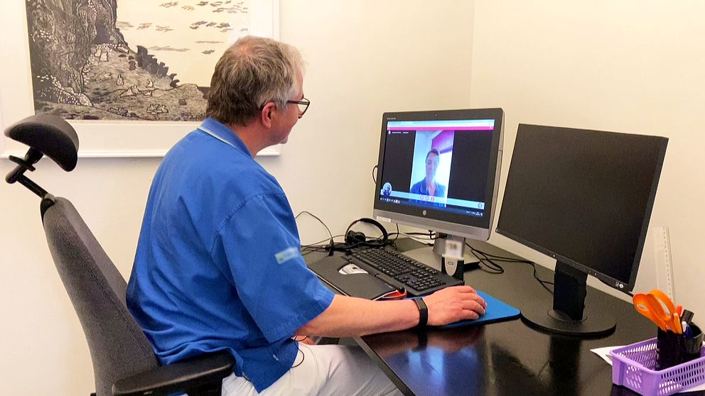 En man i blåa scrubs har ett digitalt möte framför en dator