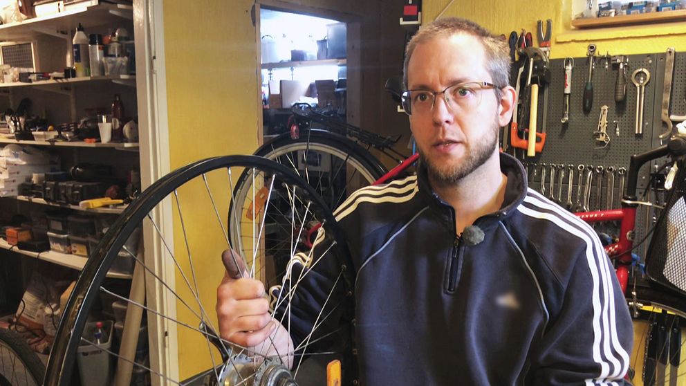 Mattias – en man i sweater och med glasögon – håller upp en cykelfälg inne i en cykelverkstad