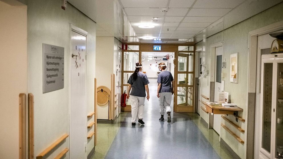 Personer i vårdkläder syns gå i en sjukhuskorridor.