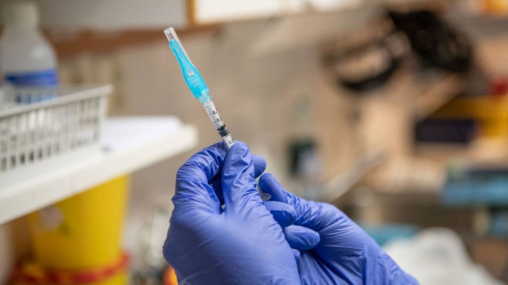 Två händer med blå plasthandskar håller i vaccinationsspruta