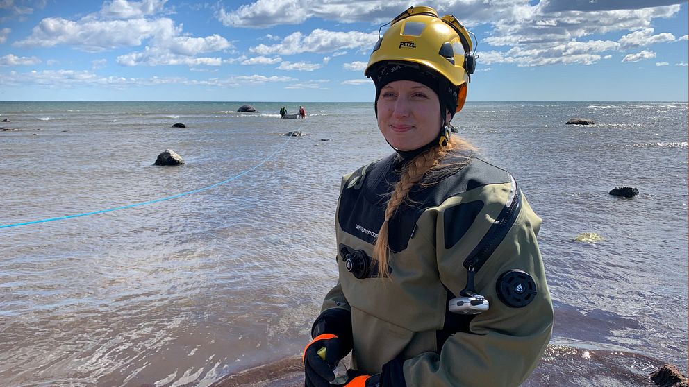 Bild på Jasmine Stavenow, biolog på SVA:s sektion för forskning och utveckling. Hon har på sig torrdräkt, handskar och en gul hjälm. Bakom henne syns havet.