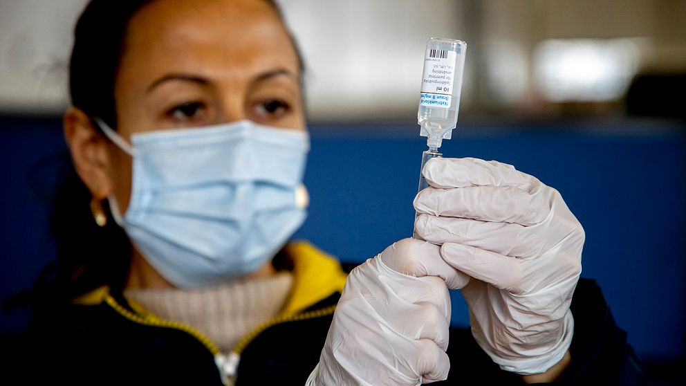 En kvinna med munskydd och handskar håller i vaccin.