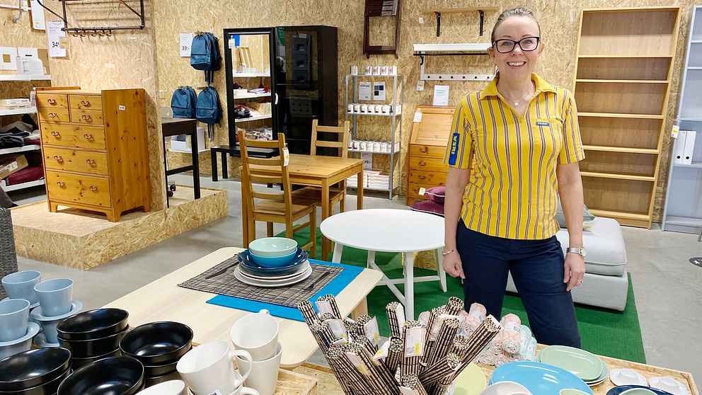 Camilla Johansson står bland en massa Ikea-möbler, iklädd gul pikétröja och glasögon. Hon ser glad ut.
