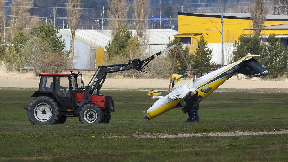 En traktor lyfter upp ett litet gulvitt flygplan som hänger uppochner i en tjock lina.