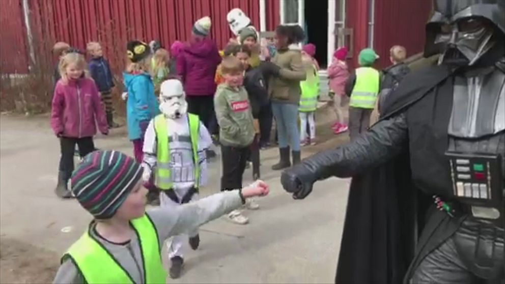 En liten pojke och en person utklädd till Darth Vader håller dina knutna nävar mot varandra. I bakgrunden syns flera barn, varav en har en vit mask på sig.