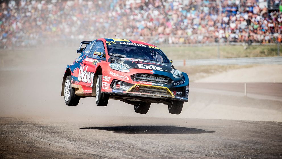 En rallycrossbil som hoppar och i bakgrunden syns ett stort publikhav.