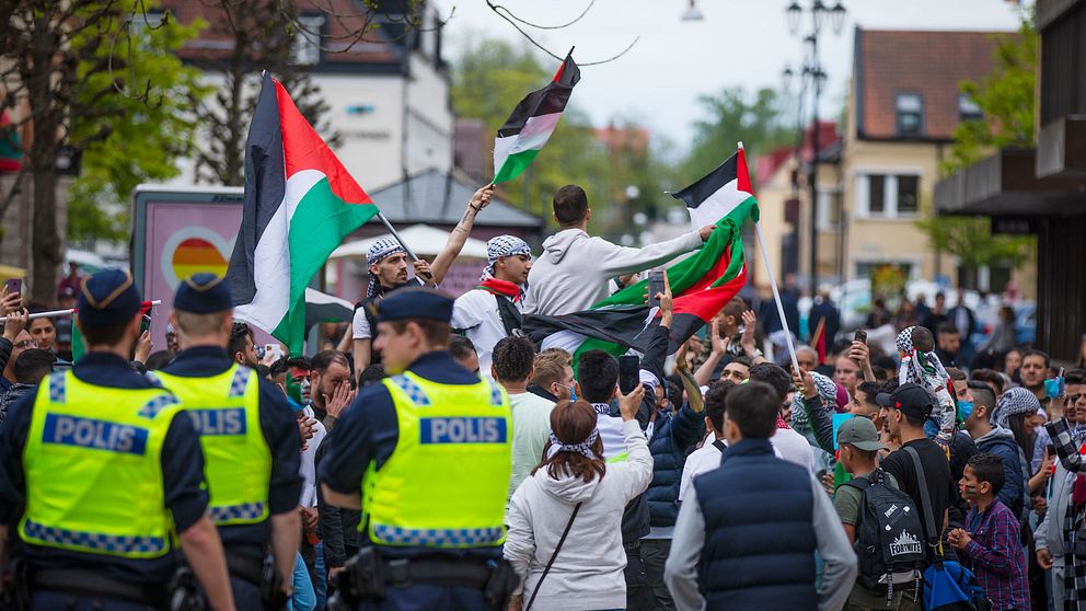 Demonstration på Stortorget i Växjö. Några av demonstranterna har palestinasjalar på huvudet och håller i den palestinska flaggan. Tre poliser står med ryggarna mot kameran.