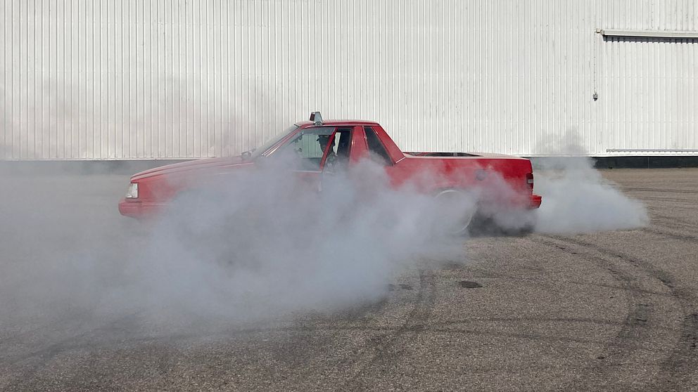 Bild på en röd A-traktor av märket Volvo som gör en burnout. Runt bilen är det vit däckrök.