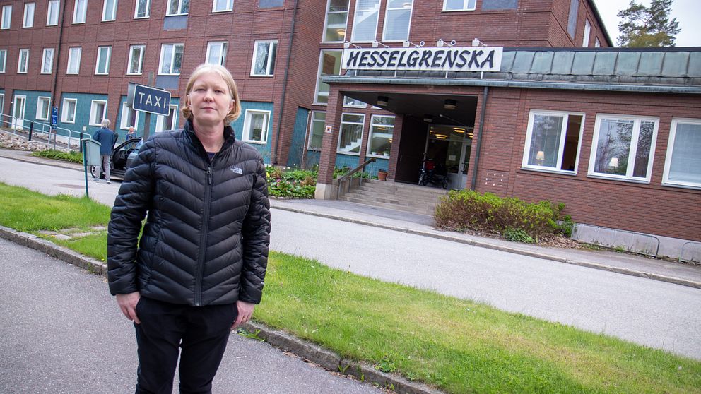 en kvinna står på gatan utanför en stor tegelbyggnad med skylten ”Hesselgrenska”