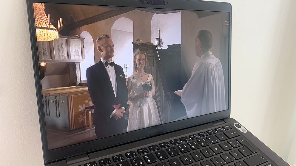 På en datorskärm syns en brudgum och brud i en kyrka framför en präst.