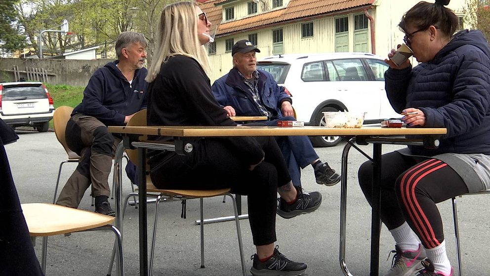 två män och två kvinnor sitter vid fikabord utomhus på en innergård