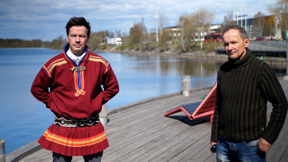 en man i samisk kolt och en något äldre man i stickad tröja står på en träbrygga i stad