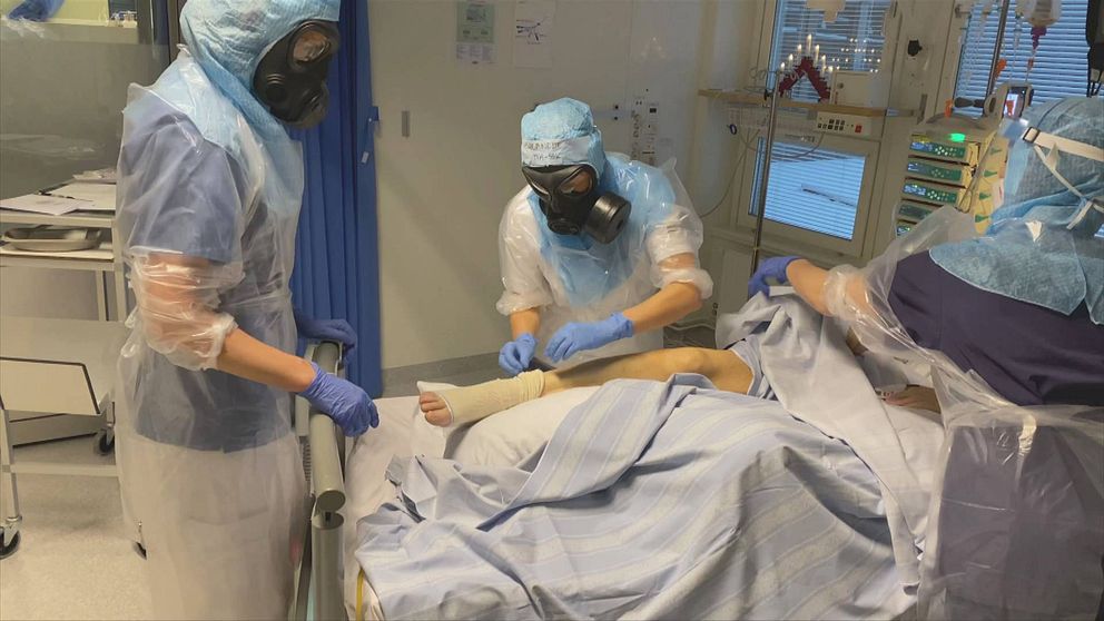 Sjukvårdspersonal i full skyddsutrustning vårdar patient på sjukhus.